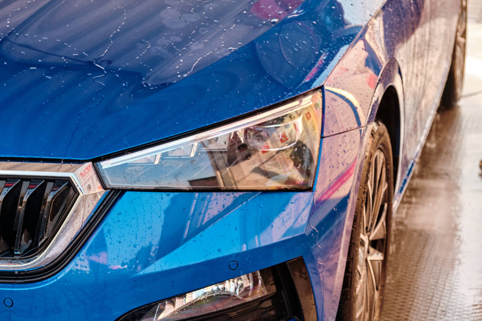Close up hood and headlight of a blue car in a drops of water after car washing. Clean car after high pressure water washing